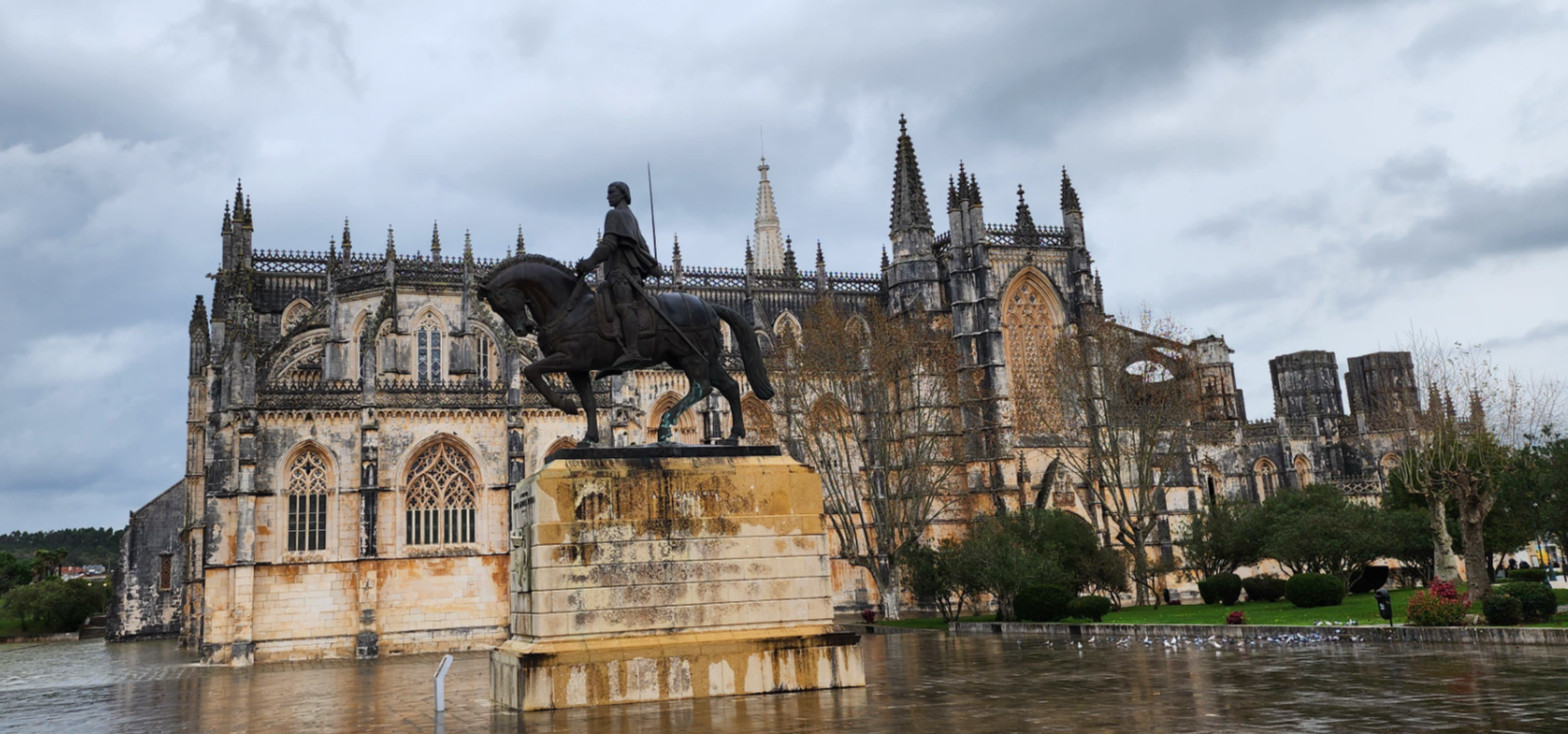 Equestrian Sentinel: A statue of a mounted figure stands guard before the majestic spires of an ancient cathedral, as grey clouds gather above, mirroring the solemn history below.